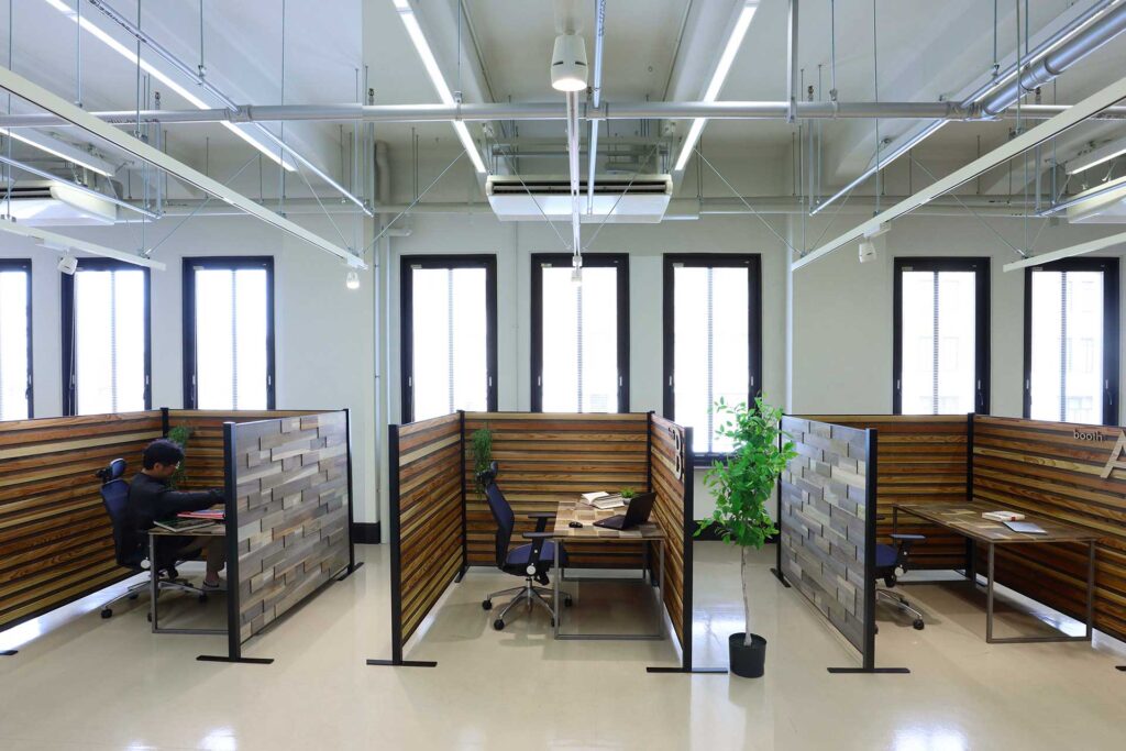広いオフィスにオシャレな木製のパーテーションでできた個人ブースを並べた風景